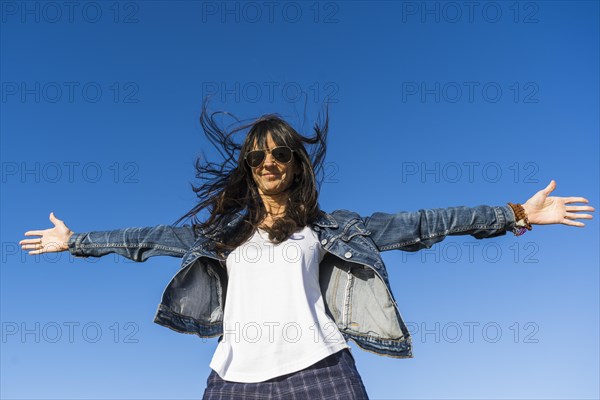Low angle view of a similing woman with her arms opened outdoors. Blue sky background