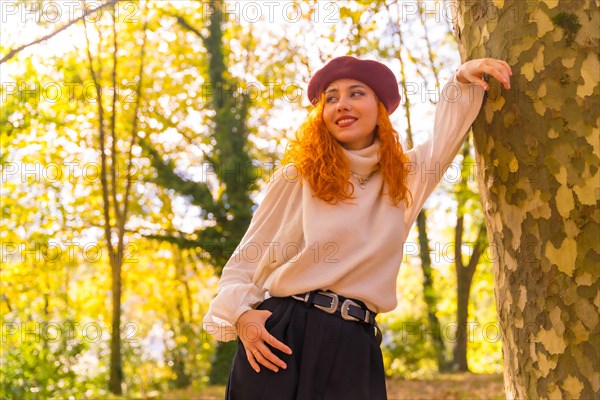 Portrait of red-haired woman leaning on a tree in a forest park
