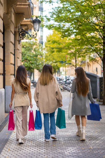 Friends from behind walking shopping on black friday with colored paper bags in hand