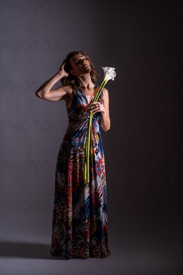 Blonde Caucasian woman in a vintage floral dress with a flower in her hand on black background