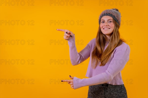 Woman in a woolen cap on a yellow background pointing to the left