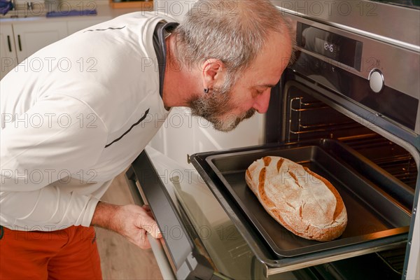 Older man with beard putting bread in the oven of his house