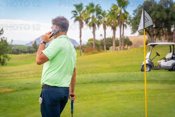 Young businessman playing golf and answering a work call with the phone from the club