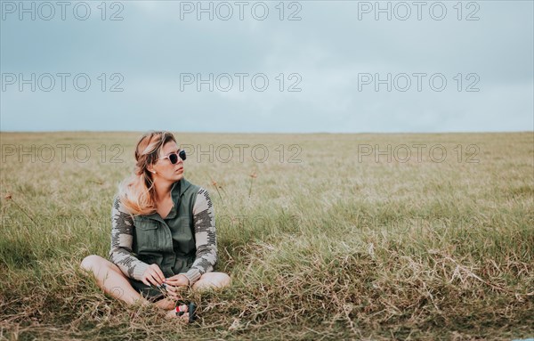 The girl is sitting cross-legged in the field