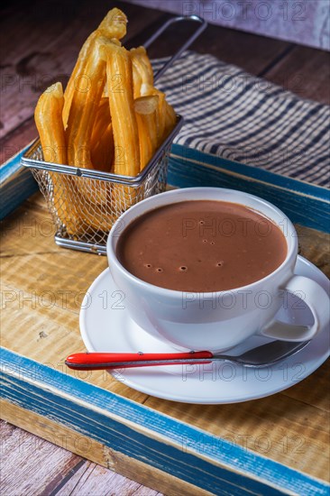 Hot chocolate in a white mug with churros in a blue wooden tray on a wooden table