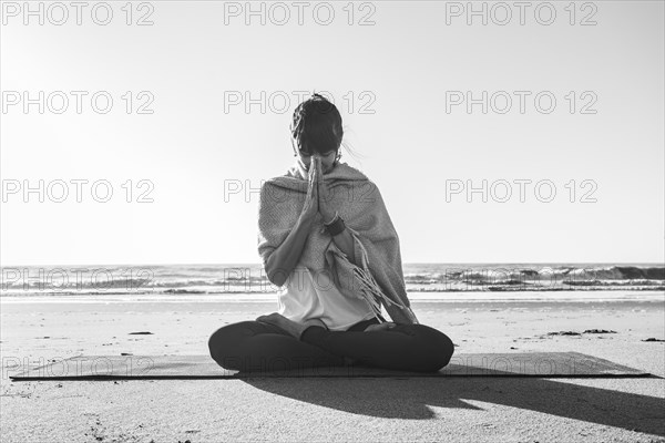 Portrait of a woman clasping hands while holding a japa mala at the beach. Namaste pose. Front view