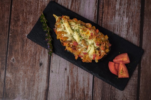 Foreground eggplant stuffed with meat and vegetables covered with bechamel sauce on a black slate on a wooden table