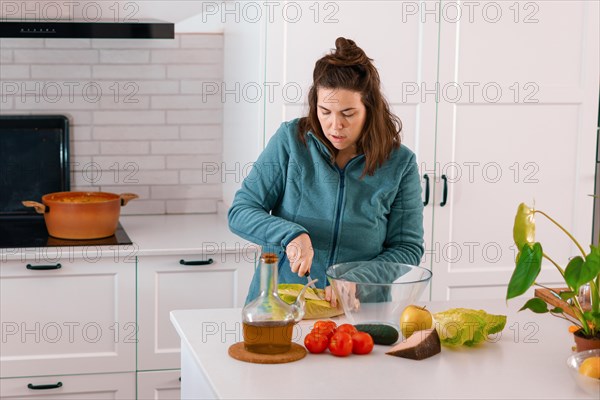 Young brunette girl chopping lettuce to prepare a salad in the kitchen