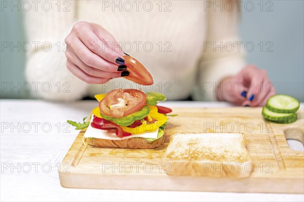 Unrecognizable person cooking a vegetable sandwich in the kitchen at home. Preparing it by putting tomato