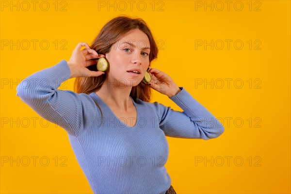 Vegan woman with earrings cucumber slices on a yellow background