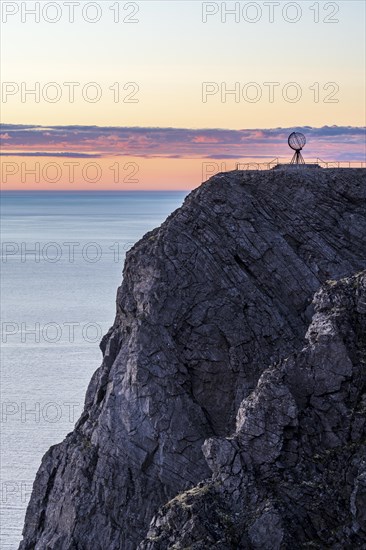 Rock cliff of the North Cape with steel globe at midnight sun