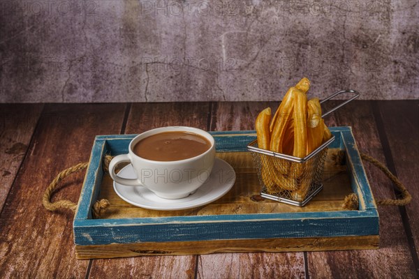 Hot chocolate in a white mug with churros in a blue wooden tray on a wooden table