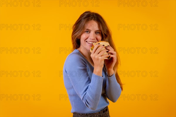Portrait of cheerful woman eating a sandwich on a yellow background
