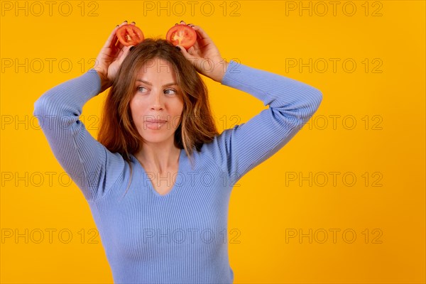 Vegan woman smiling with tomato slices on her head on a yellow background