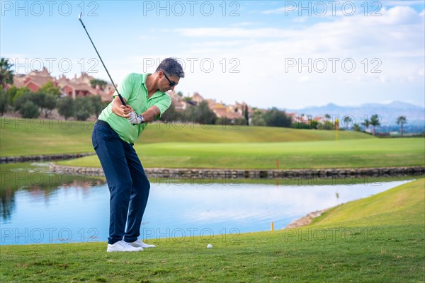 Man playing golf at golf club by a lake