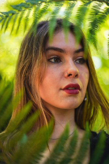 Portrait of a young brunette woman in nature in a natural park among fern leaves