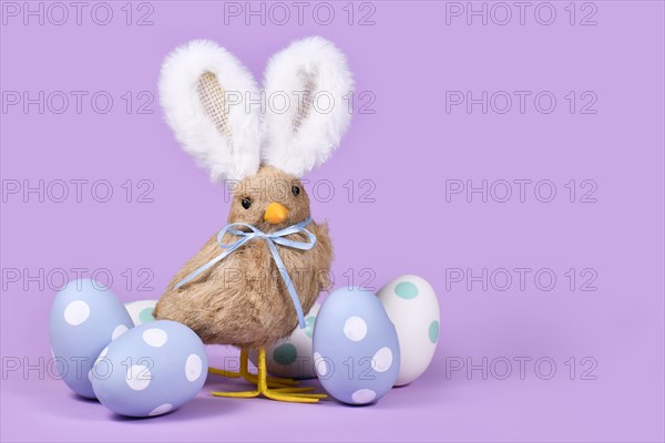 Easter chick with bunny ears and pastel Easter eggs on violet background