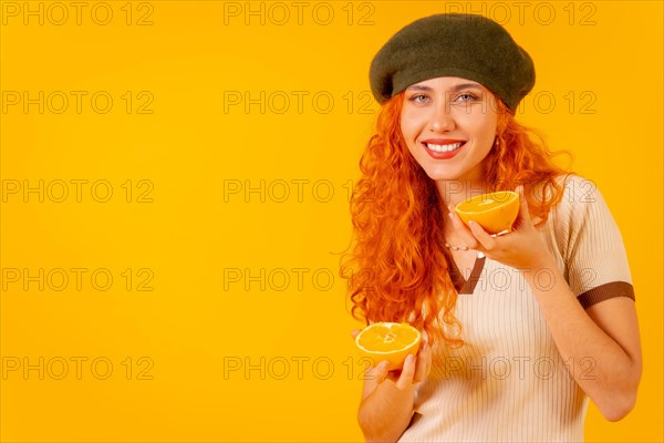 Redhead woman holding an orange over isolated yellow background