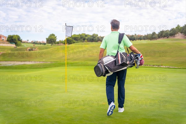 Portrait of male golfer walking down fairway carrying bags