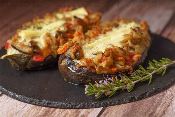 Foreground eggplant stuffed with meat and vegetables covered with bechamel sauce on a black slate on a wooden table