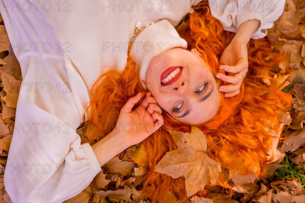 Redhead woman lying on leaves in a forest park