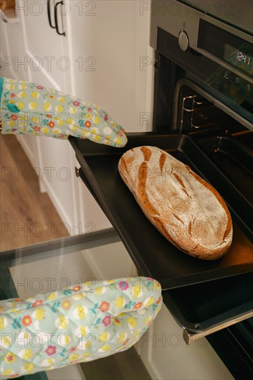 Loaf of bread in the oven tray with oven mitts