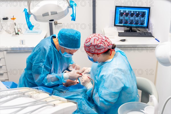 Female dentists in blue scrubs performing a complicated operation on a female patient