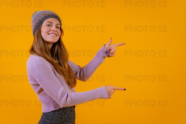 Woman with wool cap on a yellow background pointing to the right