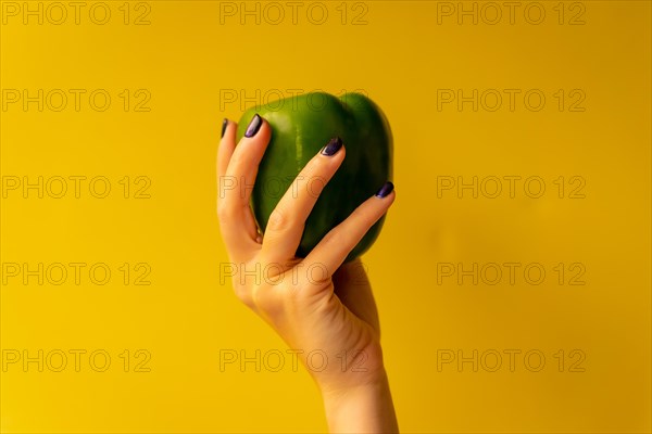 Woman's hand with a vegetable on a yellow background