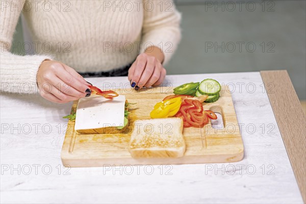 Unrecognizable person cooking a vegetable sandwich in the kitchen at home. Placing the red pepper