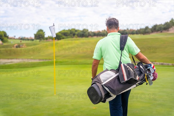 Portrait of male golfer walking down fairway carrying bags