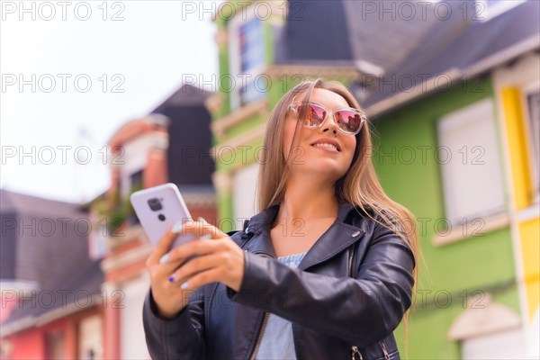 Young blonde woman in leather jacket and sunglasses smiling with the mobile