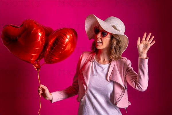Portrait of a caucasian woman enjoying dancing with a white hat in a nightclub with some heart balloons