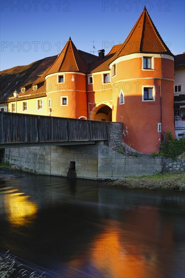 The historic orange building Biertor with the bridge over the river Regen in the evening light under a clear blue sky