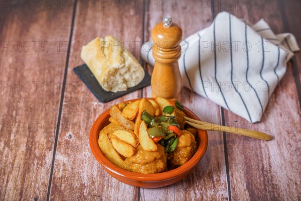 Close-up of a portion of meatballs with french fries in an earthenware casserole with covered pepper shaker and bread