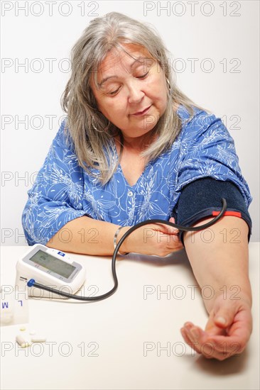 Older white-haired woman with glasses taking her blood pressure at home with white background