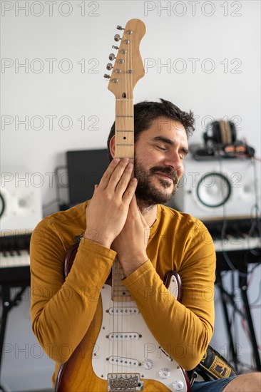 Young boy with beard playing guitar at home with piano on the back