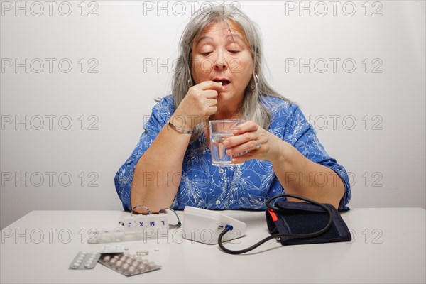 Older white-haired woman taking a pill after having her blood pressure checked