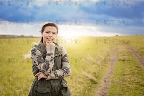 A woman on a path in the countryside sunset. Portrait of young woman with hand on chin on a beautiful country road. Smiling woman with hand on chin on a beautiful country road