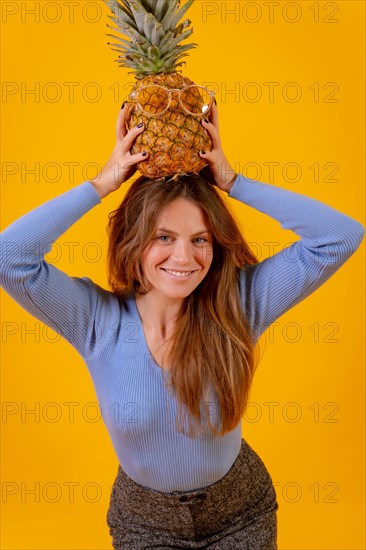 Portrait of a woman with a pineapple in sunglasses in a studio on a yellow background