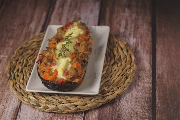 Eggplants stuffed with meat and vegetables on a white plate on a wooden table with a branch of rosemary in bloom