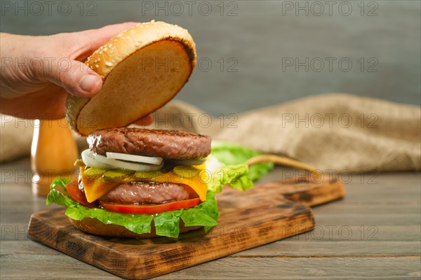 Close-up of a woman's hands opening the bun of a hamburger bun complete with two pieces of meat on a wooden board