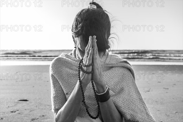 Portrait of a woman clasping hands while holding a japa mala at the beach. Namaste pose