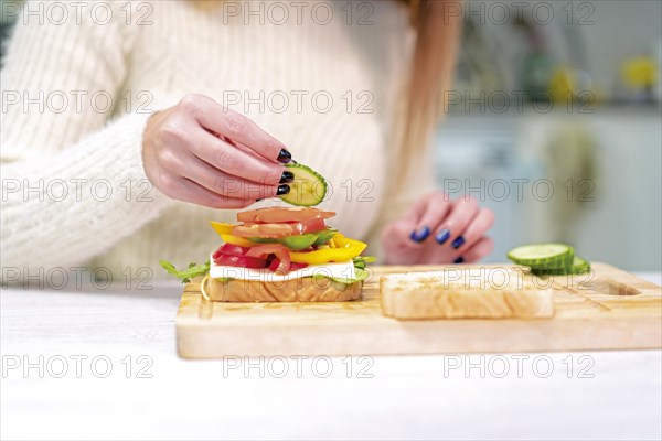 Unrecognizable person cooking a vegetable sandwich in the kitchen at home. Preparing it by putting tomato