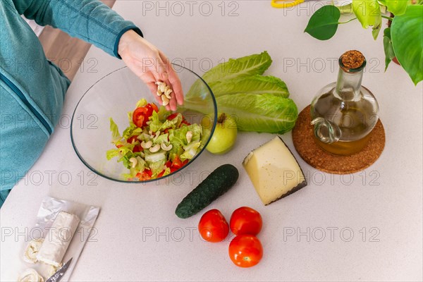 Woman adding cashews to a healthy salad at her kitchen table