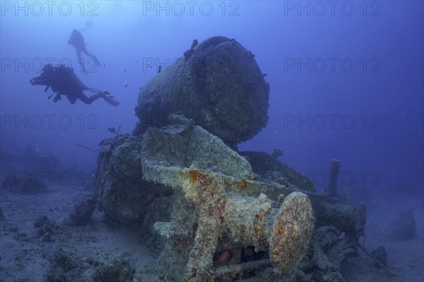 Remains of a steam locomotive from the Second World War on the seabed. Divers in the background. Dive site Thistlegorm wreck