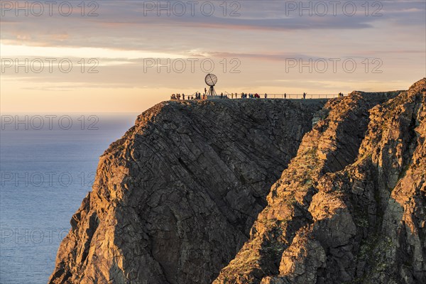 Rock cliff of the North Cape with steel globe at midnight sun