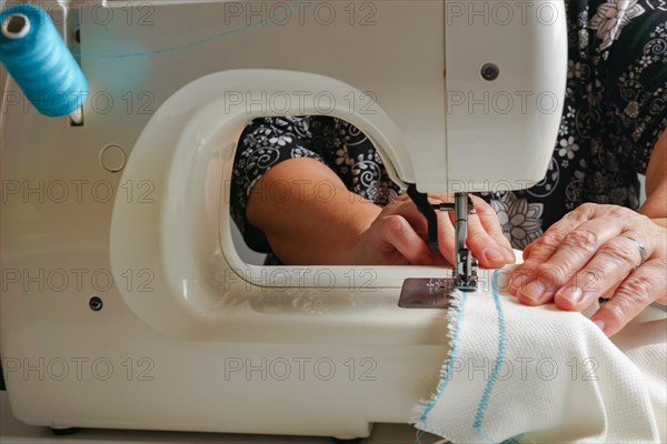 Close-up of woman's hands sewing a fabric with blue thread on a sewing machine