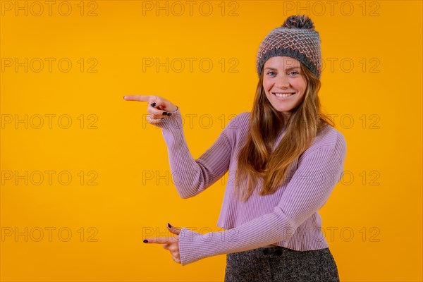 Woman in a woolen cap on a yellow background pointing to the left