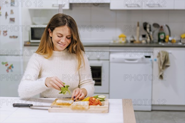 Vegetarian woman cooking a vegetable sandwich in the kitchen at home. Placing the arugula
